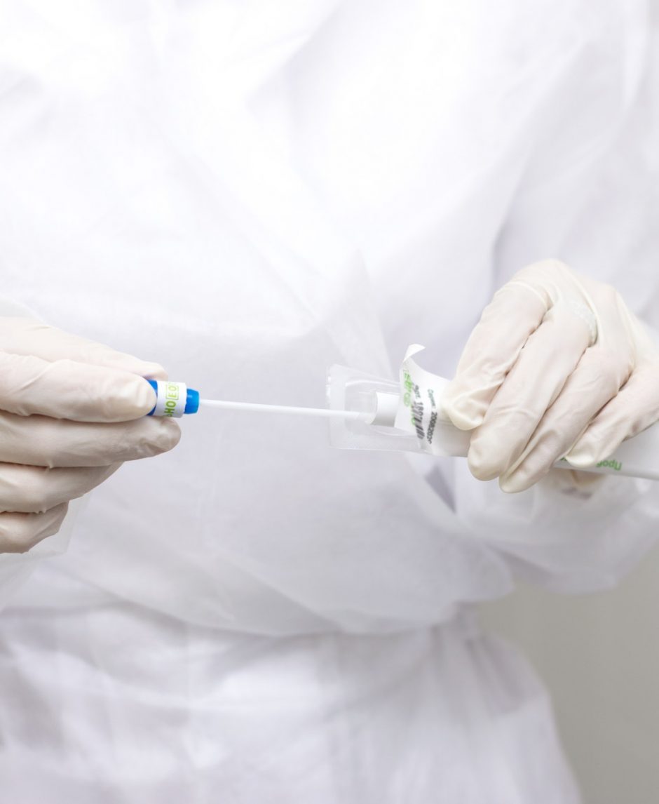 Medical worker's hands in protective clothing and gloves holding package with coronavirus test-tube.