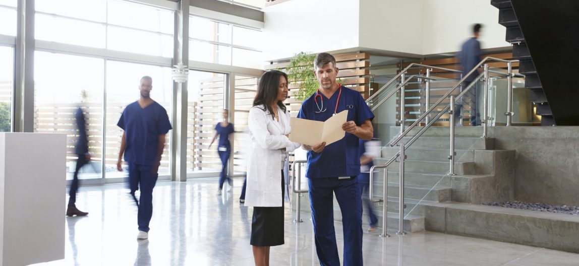 Two healthcare workers talk in the lobby of a busy hospital